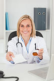 Charming blonde doctor holding prescription and medicine smiles 