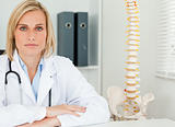 Serious blonde doctor with model spine next to her looks into ca
