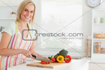 Cute woman cutting red pepper looks into camera