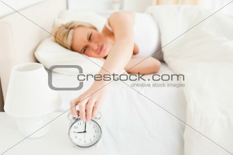 Tired woman switching off her alarm clock