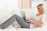 Smiling woman using a laptop while lying on a sofa