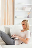 Portrait of a cute woman lying on a sofa using a laptop