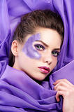 young girl laying on purple fabric wearing glitter make up