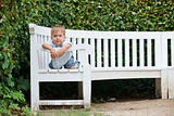 little boy sits on a bench in a park