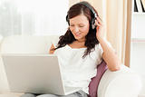 Dark-haired woman relaxing on a sofa with headphones and a notebook