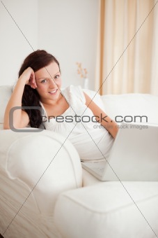 Beautiful red-haired woman relaxing on a sofa surfing the internet looking into the camera