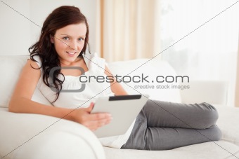 Beautiful woman relaxing on a sofa surfing the internet  with a tablet looking into the camera
