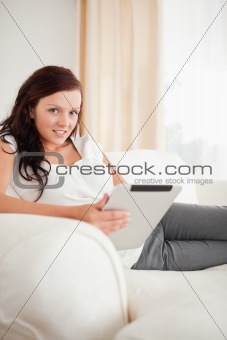 Beautiful woman relaxing on a sofa with a tablet looking into the camera