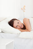Red-haired woman lying in bed smiling into camera