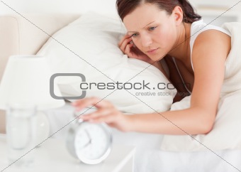 Close up of a Red-haired woman lying in bed turning off alarm clock