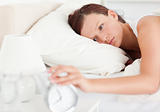 Red-haired woman lying in bed turning off alarm clock