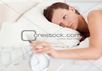 Red-haired woman lying in bed turning off alarm clock