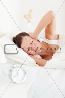 Sleepy red-haired woman lying in bed not wanting to hear the alarm clock