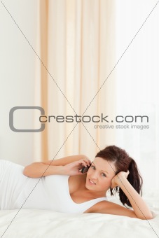 Red-haired Woman phoning on a bed looking into the camera