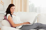 Smiling Woman with a laptop lying on a sofa