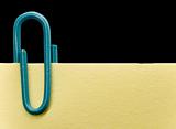 Blue paperclip on a yellow note with black background