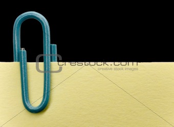 Blue paperclip on a yellow note with black background
