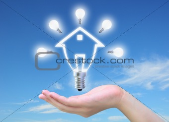 light bulb model of a house in women hand on sky