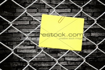 yellow note on chain link fence and old wall