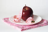 Red juicy apple and measuring tape on white plate