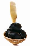 Black olives in wooden spoon on a white background.