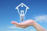 light bulb model of a house in women hand on sky