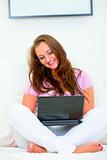 Smiling beautiful housewife sitting on sofa and using laptop
