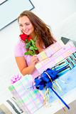 Smiling pretty woman sitting among gifts and holding rose

