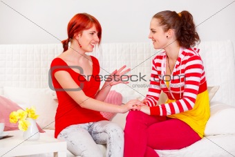 Two pretty girlfriends sitting on sofa and talking
