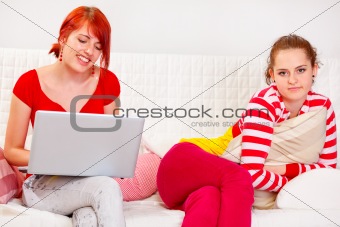 Pretty girl bored while her girlfriend using laptop
