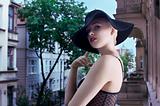 young blond fashion woman in elegant black hat  in urban backgro