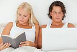 Woman reading a book while her boyfriend is using a laptop