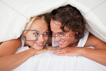 Couple under a duvet with a knowing smile