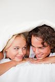 Portrait of a couple under a duvet with a knowing smile