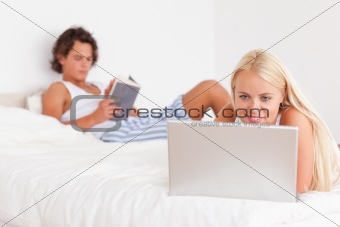 Woman using a laptop while her fiance is reading