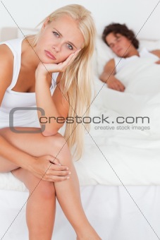 Portrait of an unhappy woman sitting on a bed while her fiance is sleeping