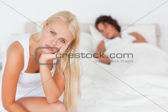 Unhappy woman sitting on a bed while her fiance is sleeping