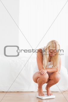 Portrait of a blonde woman squatting on a weighing machine