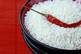 white rice in a black bowl with chili pepper on  red background