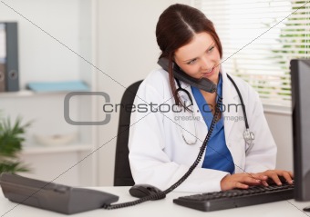 Female doctor telephoning whilst typing