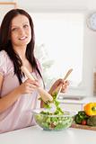 Smiling woman mixing a salad looking into the camera