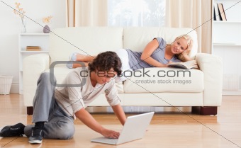 Man using a laptop while his girlfriend is holding a book