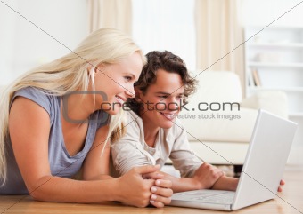 Couple using a laptop while lying on the floor