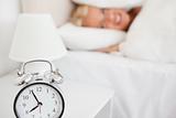 Woman hidding her head in a pillow while the alarrmclock is ringing