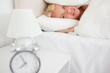 Tired woman hidding her head in a pillow while the alarmclock is ringing