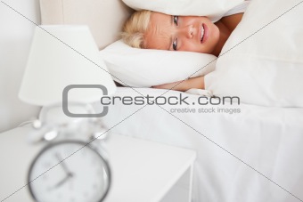 Tired woman hidding her head in a pillow while the alarmclock is ringing