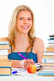 Cheerful teen girl sitting at table with lots of books
