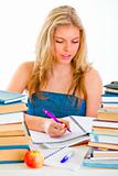 Girl sitting at table with lots of books and doing homework
