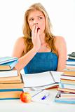 Shocked teen girl sitting at desk with piles of books
