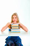 Concentrated girl sitting at desk and holding hands on piles of books
